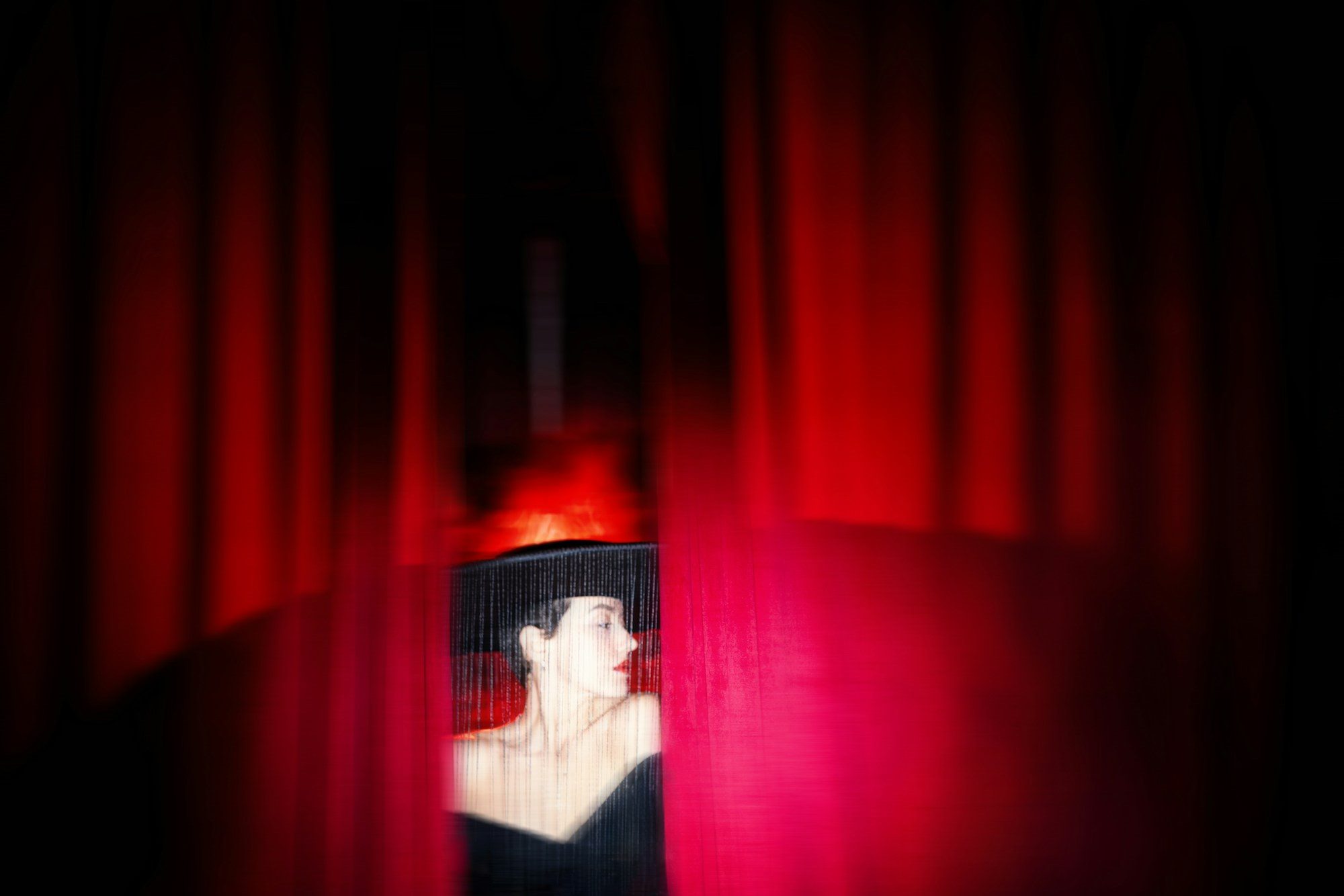 A child looking out from behind a red stage curtain